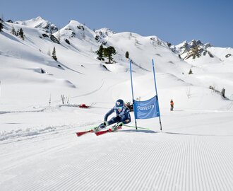 A ski racer carves through a slalom gate in deep turn on sunny day with powder snow. | © Gasteinertal Tourismus GmbH, Marktl Photograhpy