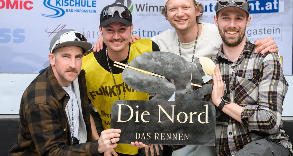 Four men smile holding “Die Nord – Das Rennen” trophy in front of sponsor wall in Gastein. | © Gasteinertal Tourismus GmbH, Marktl Photograhpy