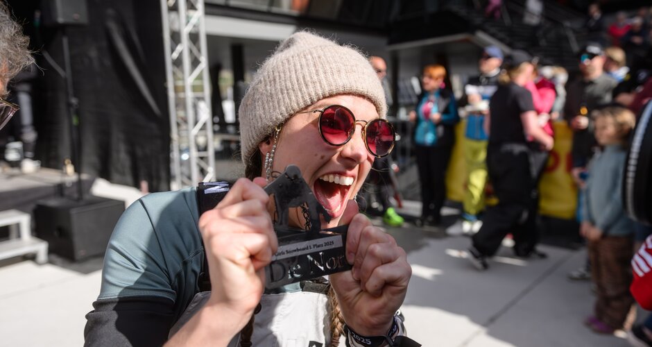 Cheering snowboarder proudly holds up her trophy at “Die Nord – Das Rennen” 2025. | © Gasteinertal Tourismus GmbH, Marktl Photograhpy