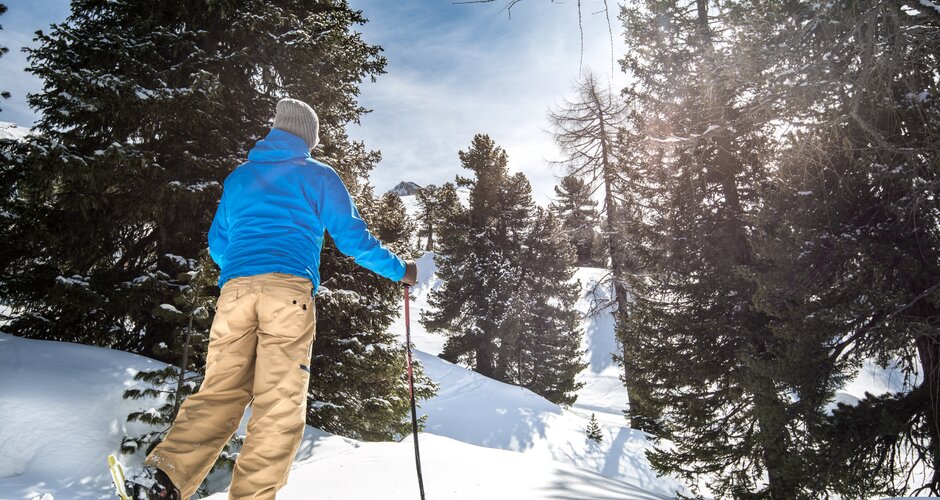 Man with blue winter jacket, grey bonnet and beige trousers walks by with snowshoes in deep snow near isolated trees | © Gasteinertal Tourismus GmbH, Marktl