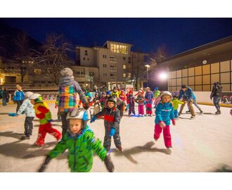 Lots of children and a few adults romp around on an ice rink