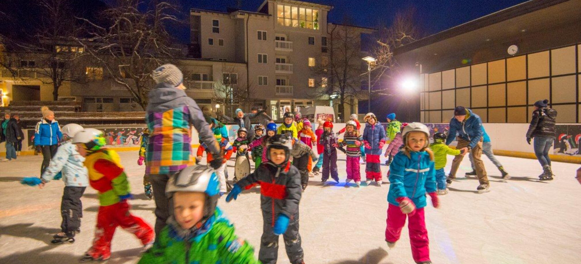 Lots of children and a few adults romp around on an ice rink