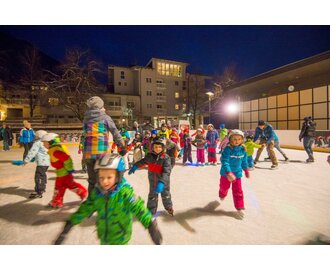 Lots of children and a few adults romp around on an ice rink