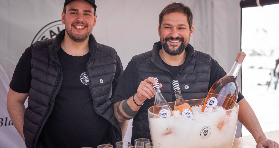 Two men behind a booth with Rosalia DAC rosé wine in an ice bucket and several wine glasses