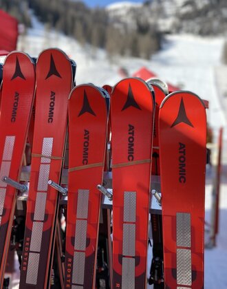 Red Atomic ski pairs leaning against a ski rack