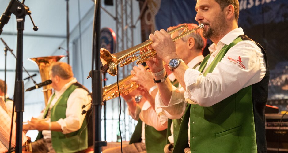 The flugelhorn player of the music group "Innsbrucker Böhmischen" is playing while two of his fellow musicians can also be seen playing in the background. | © Harald Steiner 