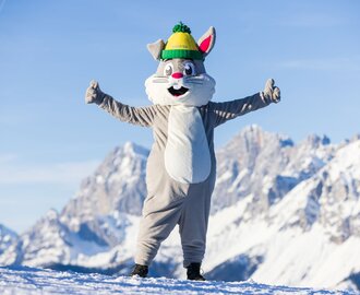 Hopsi the mascot is standing on the piste with both arms outstretched with his thumbs up | © Martin Huber
