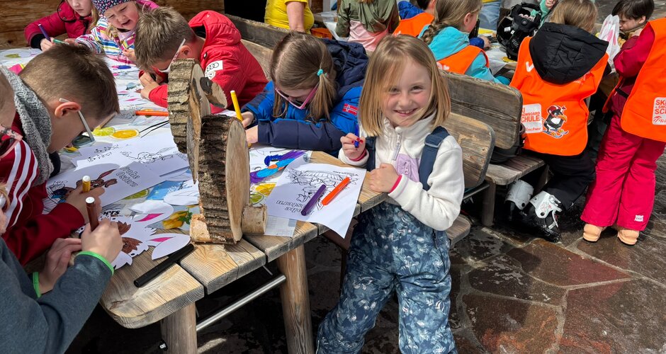 Several children sit at wooden tables colouring drawings during a kids programme at the ski area | © Planai