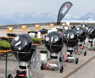 Row of black kettle grills with gear on a terrace overlooking a mountain panorama. | © Harald Steiner