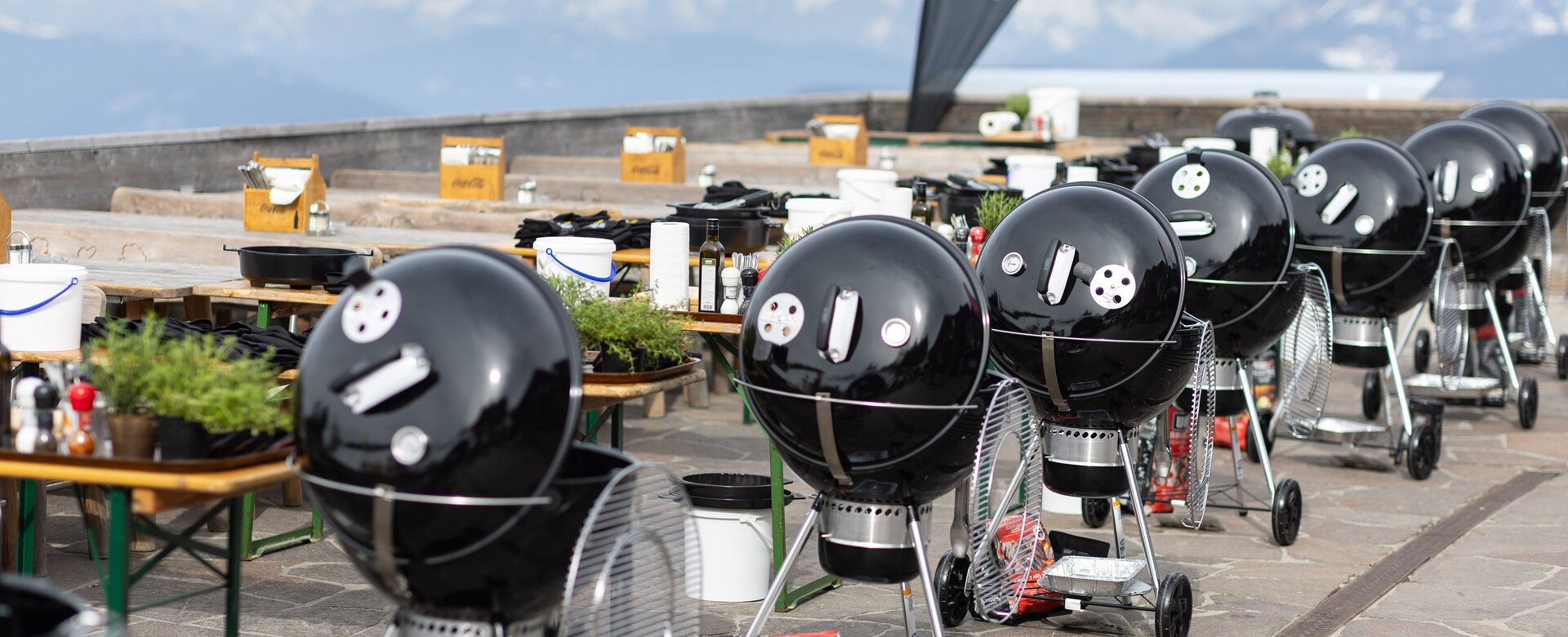 Row of black kettle grills with gear on a terrace overlooking a mountain panorama. | © Harald Steiner