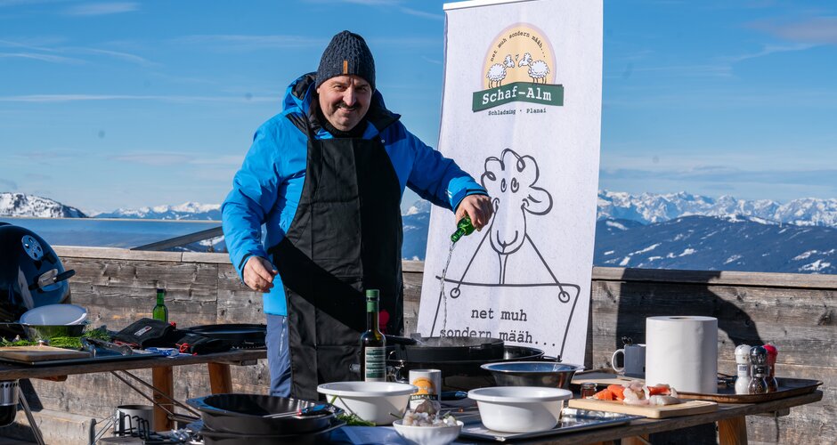 Johann Lafer grills outdoors on the Planai with snowy Alps behind. | © Mario Egger