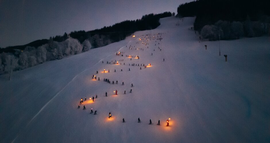 Children ski with torches down Reiteralm at night, glowing orange lights in the snowy darkness | © Gerald Grünwald