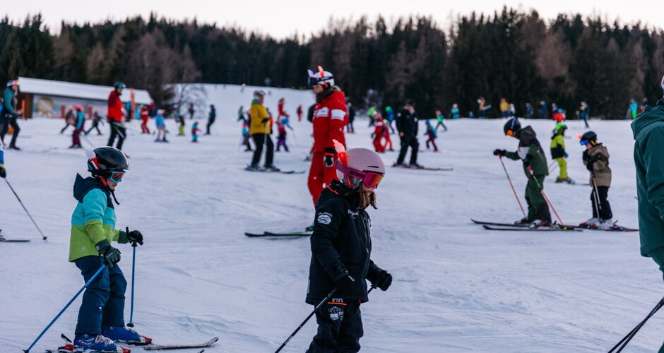 Many children ski in groups at dusk on Reiteralm, accompanied and guided by ski instructors | © Gerald Grünwald