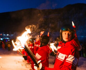 Young torchbearers in red ski suits stand in snow during nighttime New Year’s Eve celebration | © Gerald Grünwald
