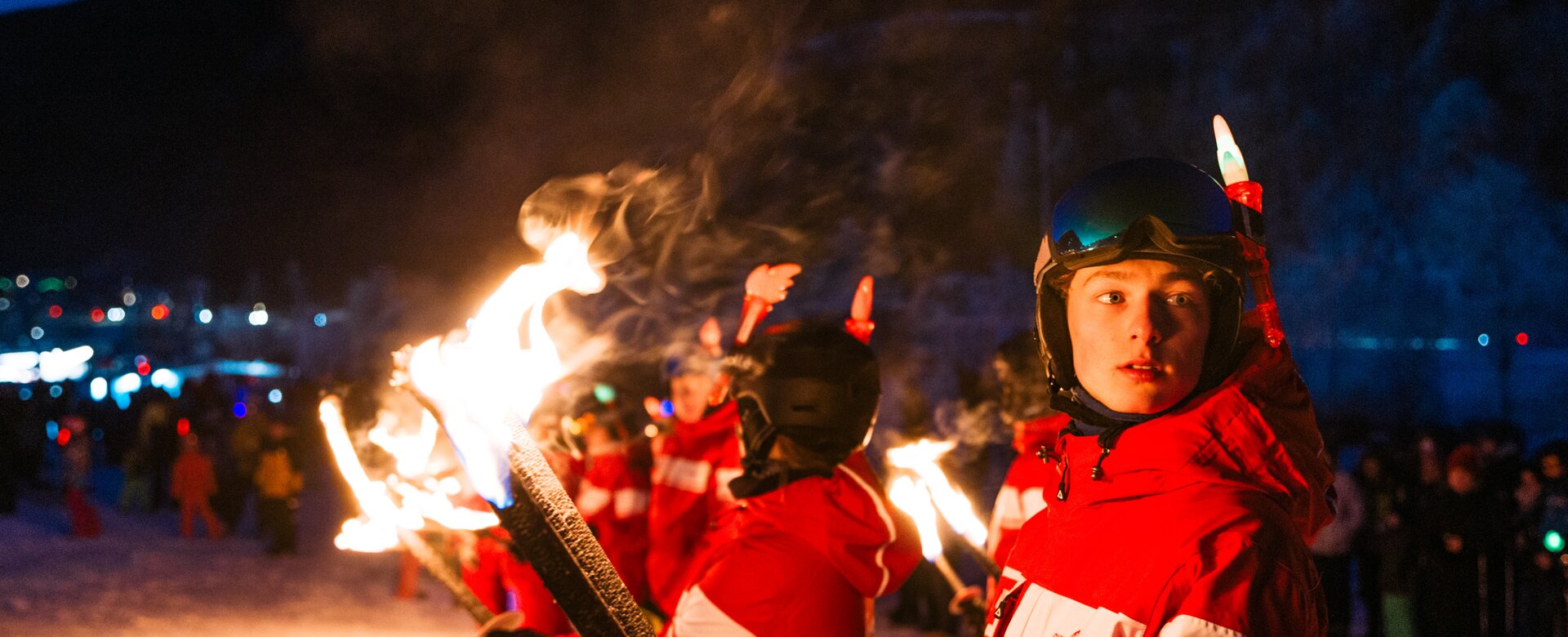Young torchbearers in red ski suits stand in snow during nighttime New Year’s Eve celebration | © Gerald Grünwald