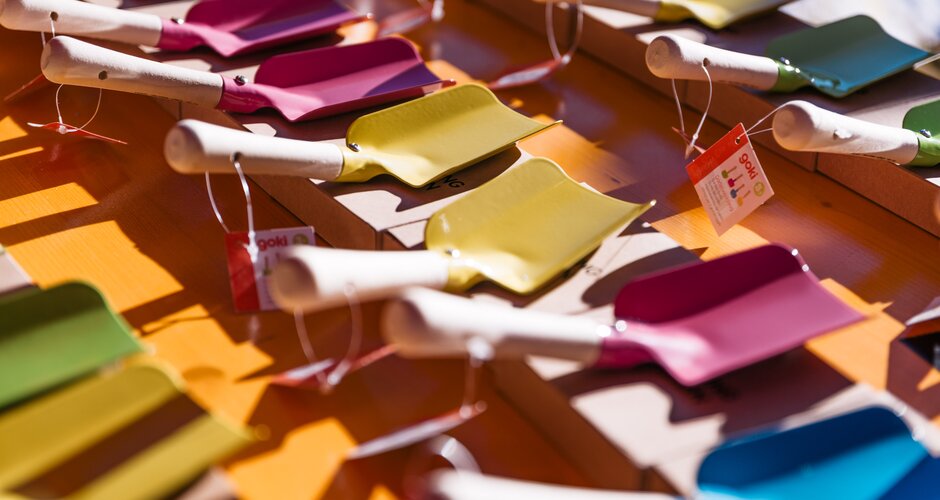 Several small metal shovels in bright colours are laid out on a table in the sunlight | © Gerald Grünwald
