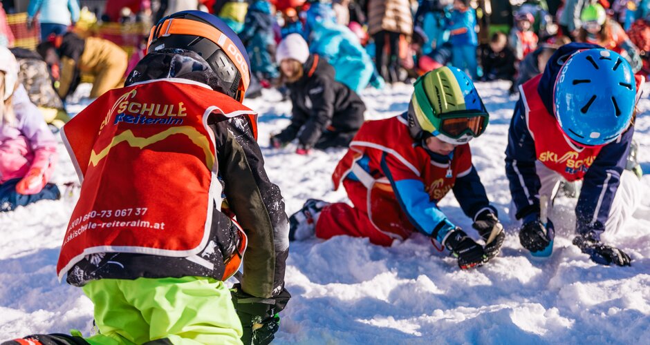 Children in red vests dig in the snow with small tools during the Reiteralm ski school treasure hunt | © Gerald Grünwald