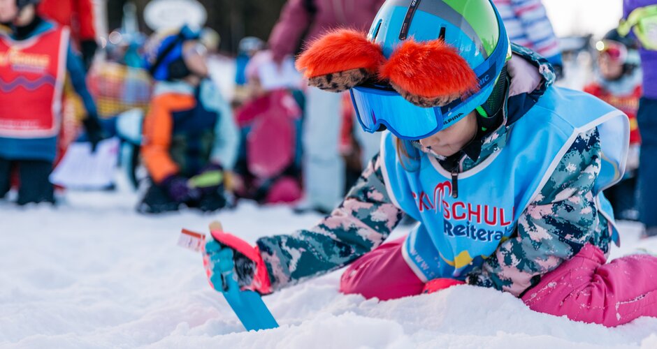 A child kneels in the snow with a shovel, digging during a treasure hunt at Reiteralm | © Gerald Grünwald