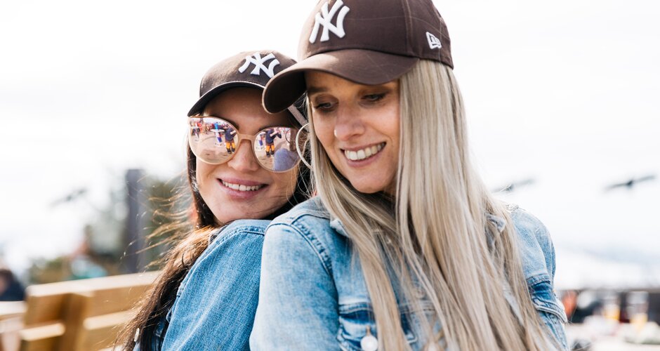 Two young women in denim jackets and caps smile in the sun during a spring event on Reiteralm | © Gerald Grünwald