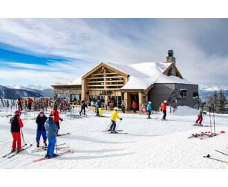 Exterior view of a modern ski hut with lots of skis out front and skiers passing by | © Christian Steiner