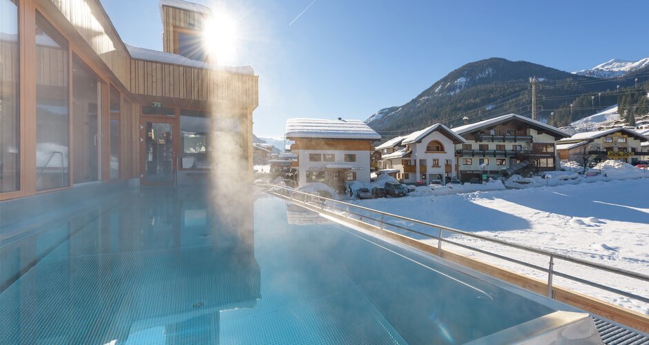 Steaming outdoor pool with wooden facade and snowy mountains in the background