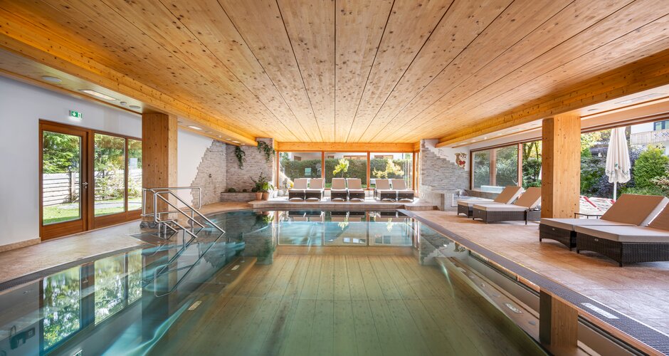 Indoor pool at Tirolerhof with wooden ceiling, stone wall, loungers and windows