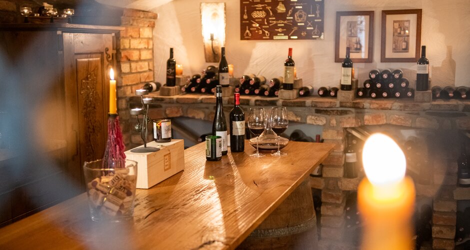 Wine bottles, glasses and candles on barrel table in brick wine cellar
