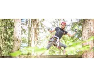 Young woman with helmet balances on rope in Gröbming’s adventure park high ropes course between forest trees | © Christoph Huber