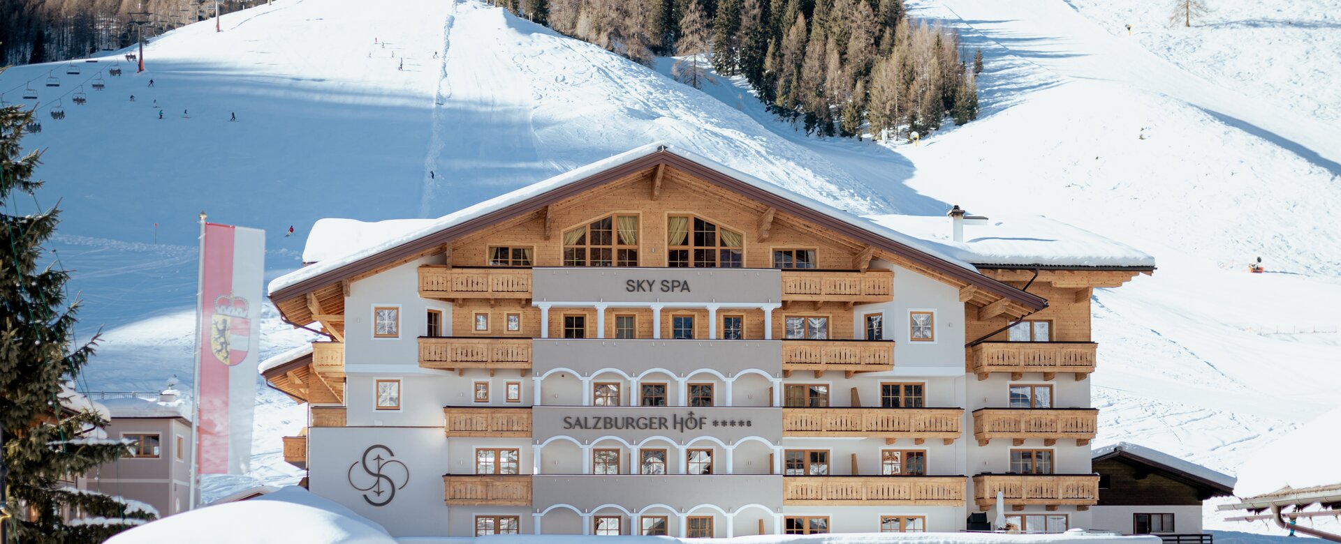 Hotel Salzburger Hof with wooden facade in front of snowy slope and ski lift | © Nadia Jabli