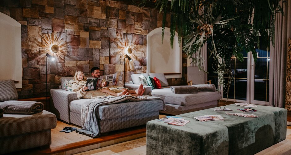 Man and child reading in spa on lounger in front of stone wall and hanging plants | © Nadja Jabli