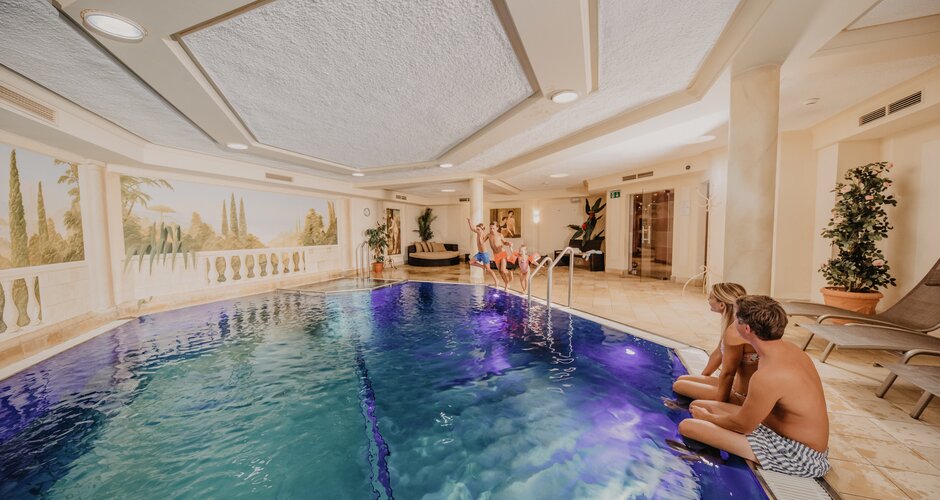 Children jump into lit indoor pool while parents sit at the pool edge | © Nadia Jabli