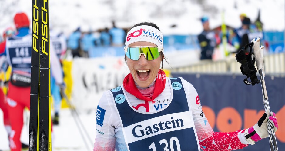 Smiling skier with bib number 130 holds skis and poles toward the camera in the finish area at Gastein. | © Gasteinertal Tourismus, Mangotree Photography