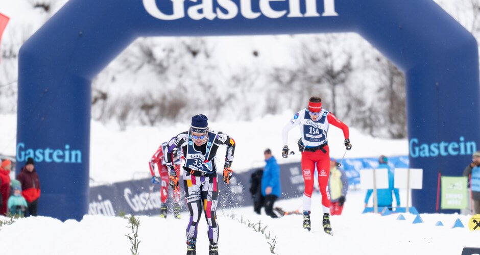 Two skiers in a final sprint beneath the Gastein arch, snow spraying as they race toward the finish. | © Gasteinertal Tourismus, Mangotree Photography