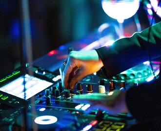 Close-up of hand on mixer with colourful lights during DJ set at night-time festival