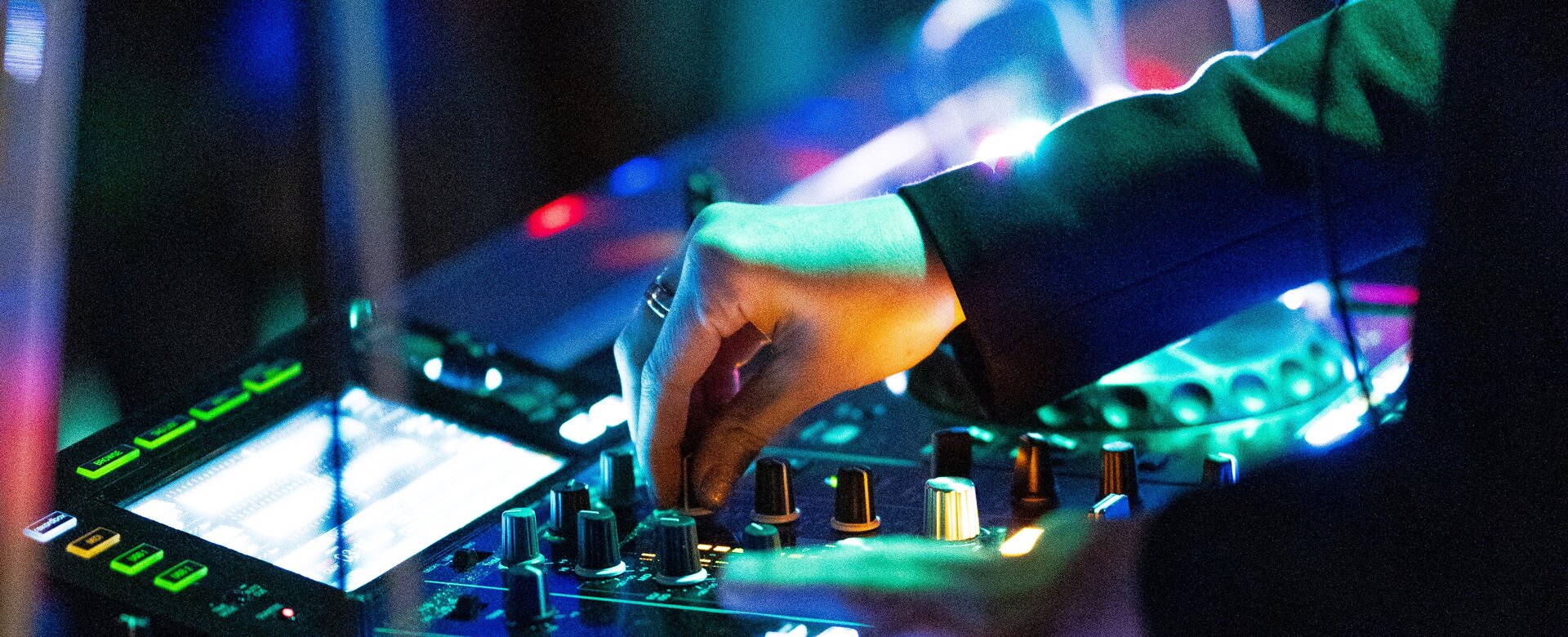 Close-up of hand on mixer with colourful lights during DJ set at night-time festival