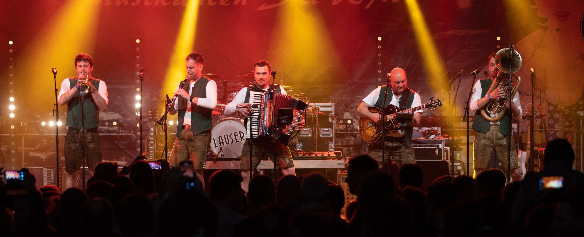 Five musicians are on stage while a big poster with "Musicians Ski World Cup" hangs in the background and the crowd sings along. | © Harald Steiner