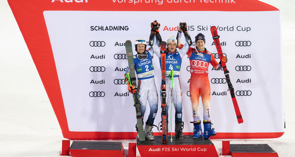 Three ski racers cheer on the winners' podium at Nightrace Schladming in front of sponsor wall | © Martin Huber