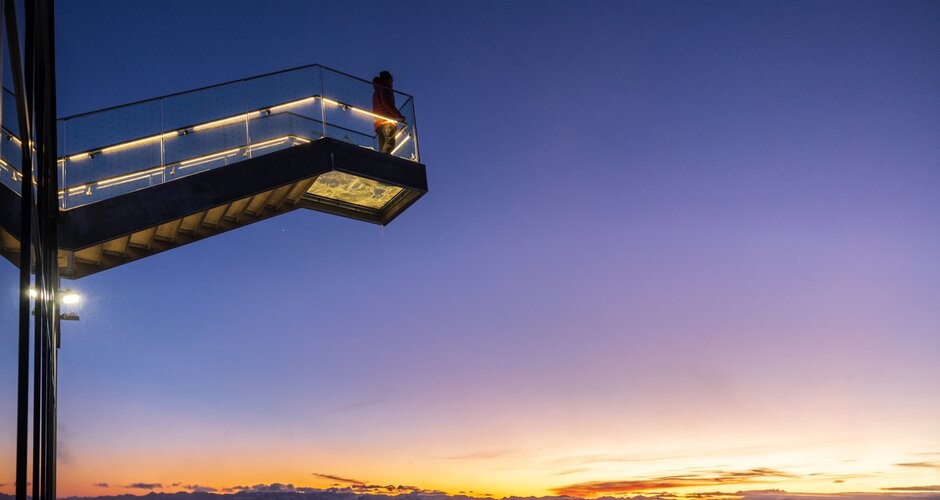 Person stands on illuminated skywalk on Dachstein during vibrant sunset above mountain landscape | © Martin Huber