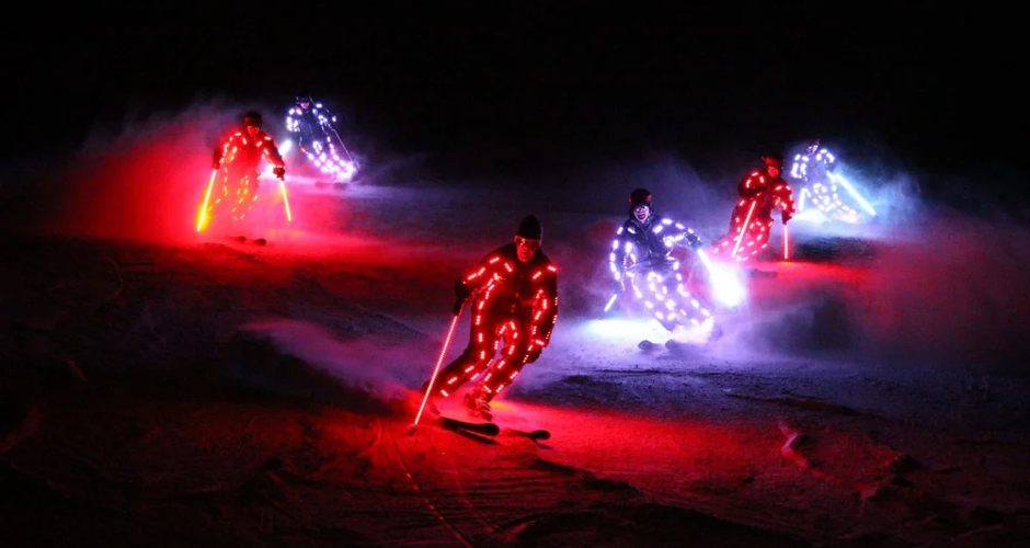 5 skiers with white and red lights on their ski suits and ski poles ski down the piste in a formation | © Erlebnis Rittisberg