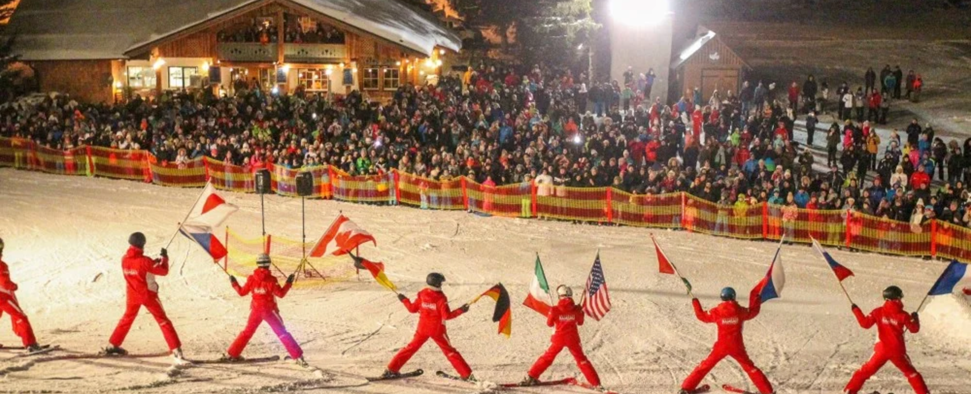 Skifahrer fahren auf einer beleuchteten Piste mit Fahnen in den Händen auf die Menschen im Zielhang unten zu | © Erlebnis Rittisberg