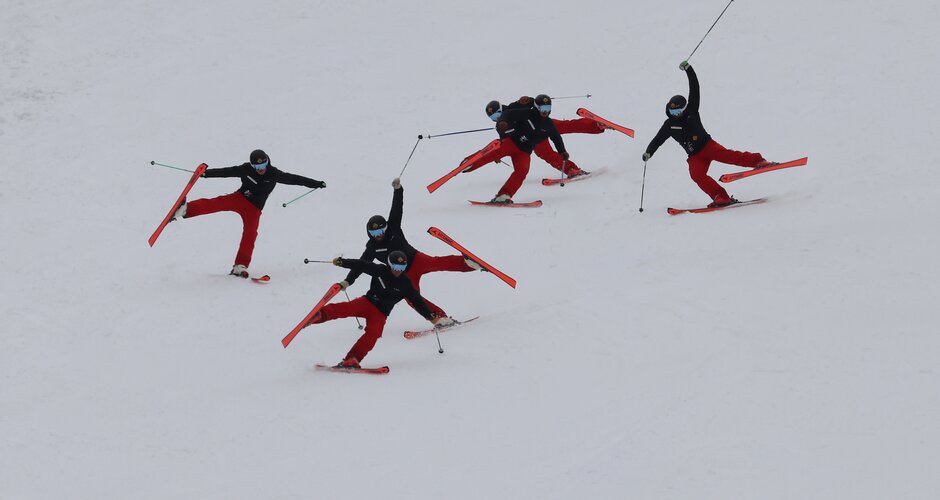 Five skiers perform synchronized lift moves with arms and legs extended on the slope | © Michael Simonlehner