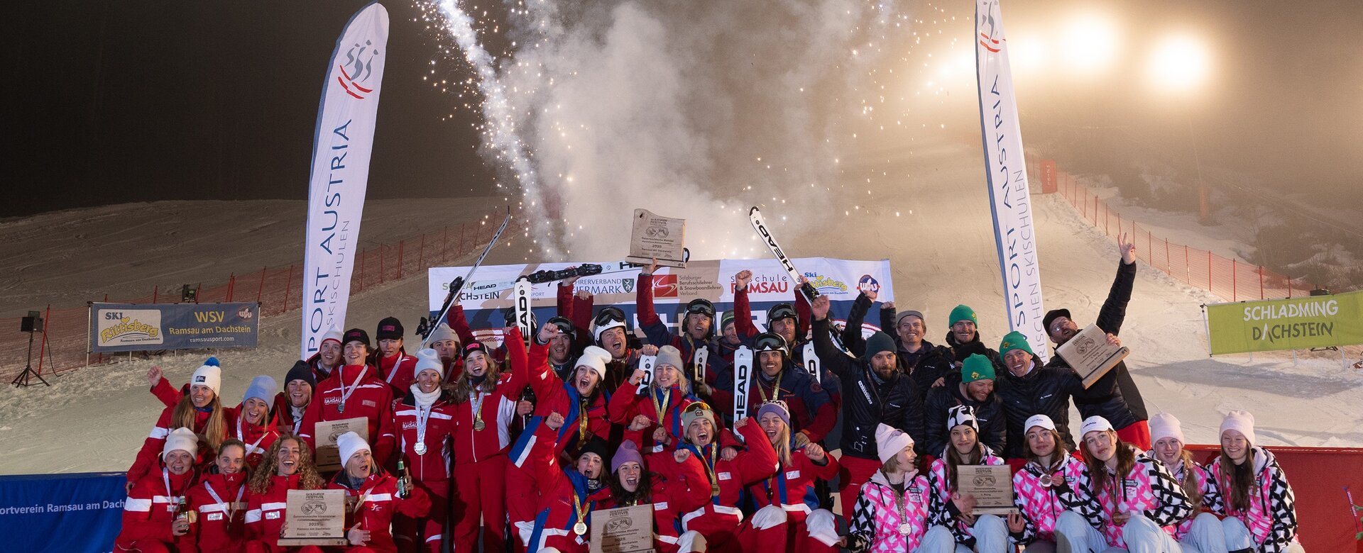 Large winning group poses in front of fireworks and banners on a night ski slope | © Michael Simonlehner