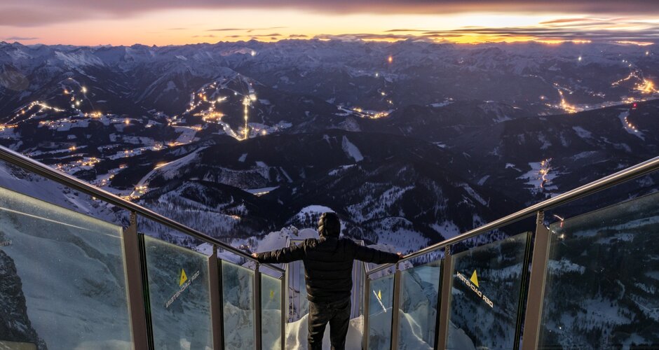 Person stands on Dachstein viewing platform overlooking lit valley at nightfall | © Martin Huber