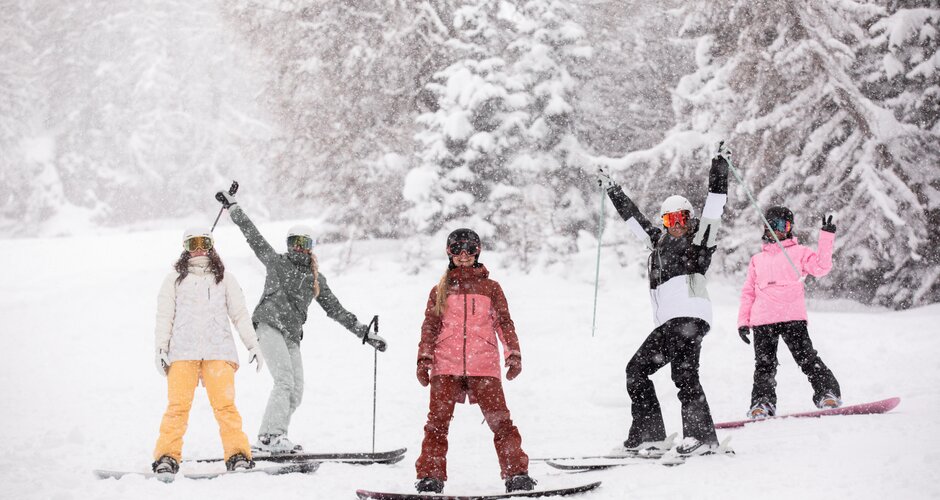 Five girls stand on the piste, either on skis or on a snowboard, and smile while it snows | © QParks
