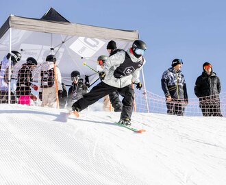 Freestyle skier skis away from the start and the next participants are already gathered under the tent at the start | © Hannes Mautner