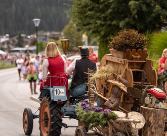 A tractor with a traditionally dressed couple pulls a rustic heritage cart through the village during a cattle drive. | © ©bymichaelgroessinger_www.filzmoos.at