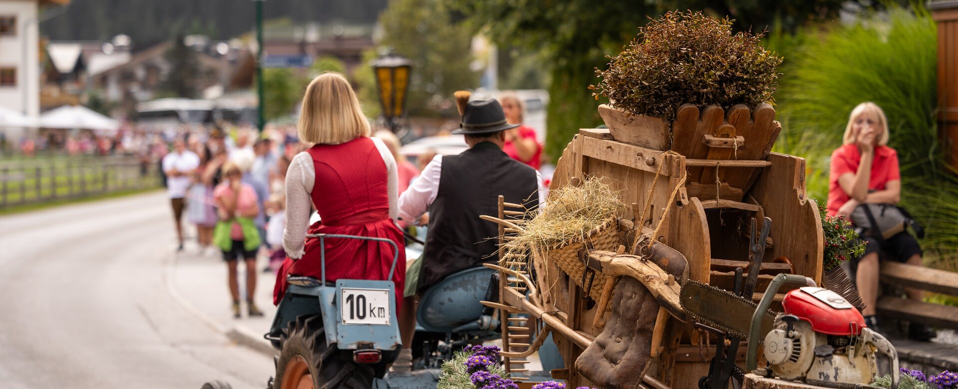 A tractor with a traditionally dressed couple pulls a rustic heritage cart through the village during a cattle drive. | © ©bymichaelgroessinger_www.filzmoos.at