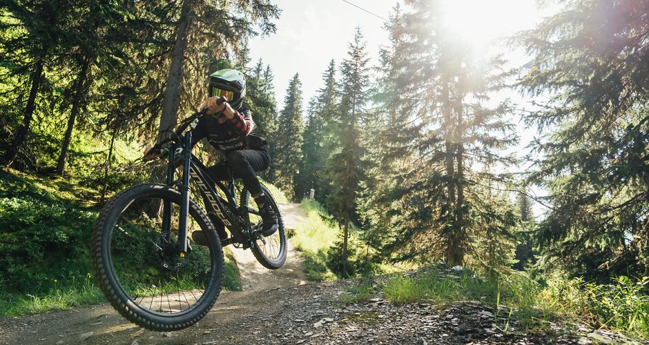 Mountain biker speeds along the trail at Bikepark Schladming, with sunlight shining through the trees. | © Bartek Pawlikowski