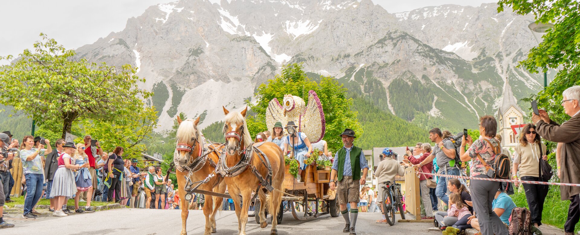 Decorated horse-drawn wagon with flower display parades past crowd with Dachstein mountains behind at Spring Festival of Horses | © Simone Raninger