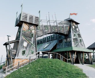 Tilted wooden fortress with bridge and turrets at Geisterberg, green shutters and red flag fluttering | © JOSalzburg